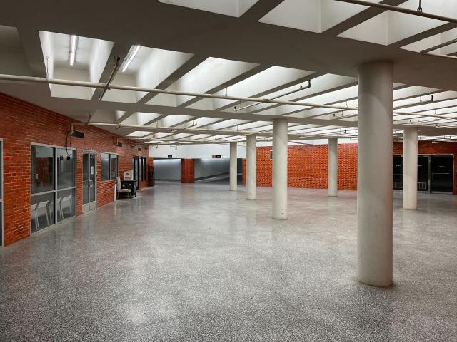 An empty room, with poles supporting the ceiling. The ceiling has holes for fluorescent lights. There is a gray lino floor.